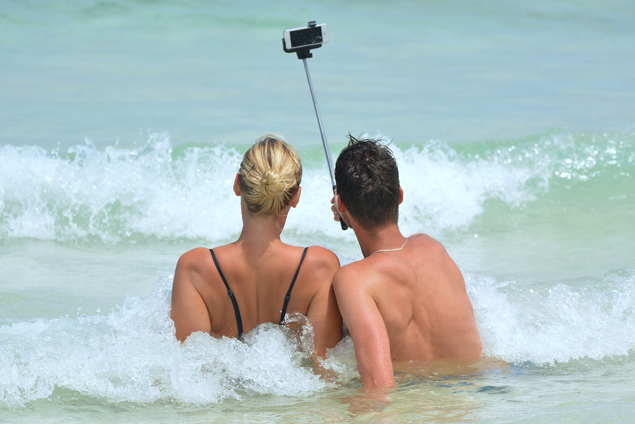 a man and a woman with a selfie stick on the beach