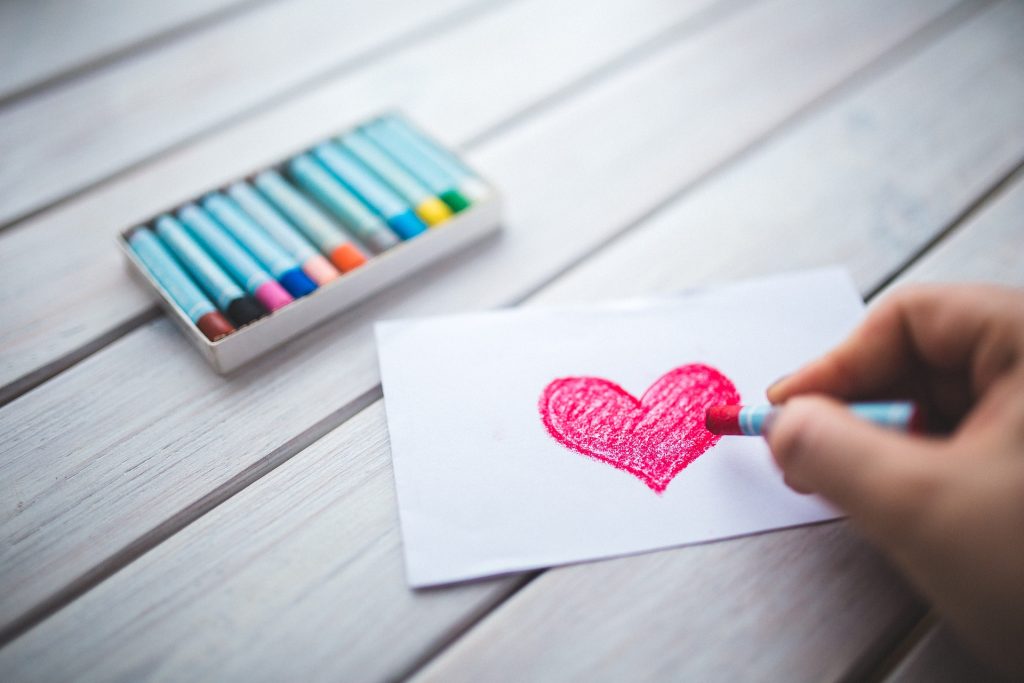 Crayons with paper with a red heart drawn on it