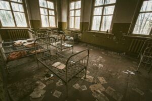 The inside of an empty room in an asylum with empty bed frames
