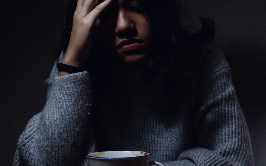 Treatment Resistant depression: a woman sitting in a darkened room with one hand on the side of her head