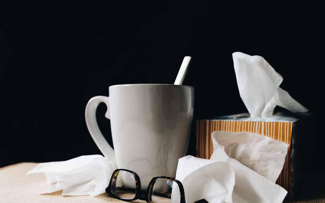 A tea cup standing next to a pair of glasses, a box of kleenex and tissue paper on a table