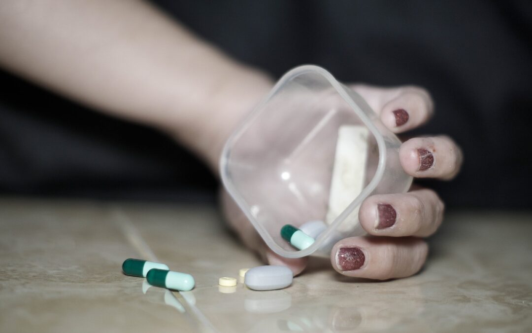 View of the hand of a person holding an open bottle with pills on the table