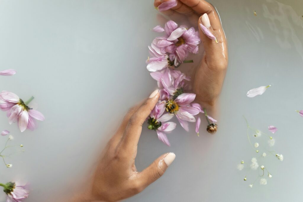 Light brown hands in a milk bath hold pink flowers. 
