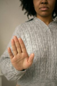 Black person wearing a grey sweater holds their hand up, as if saying stop.