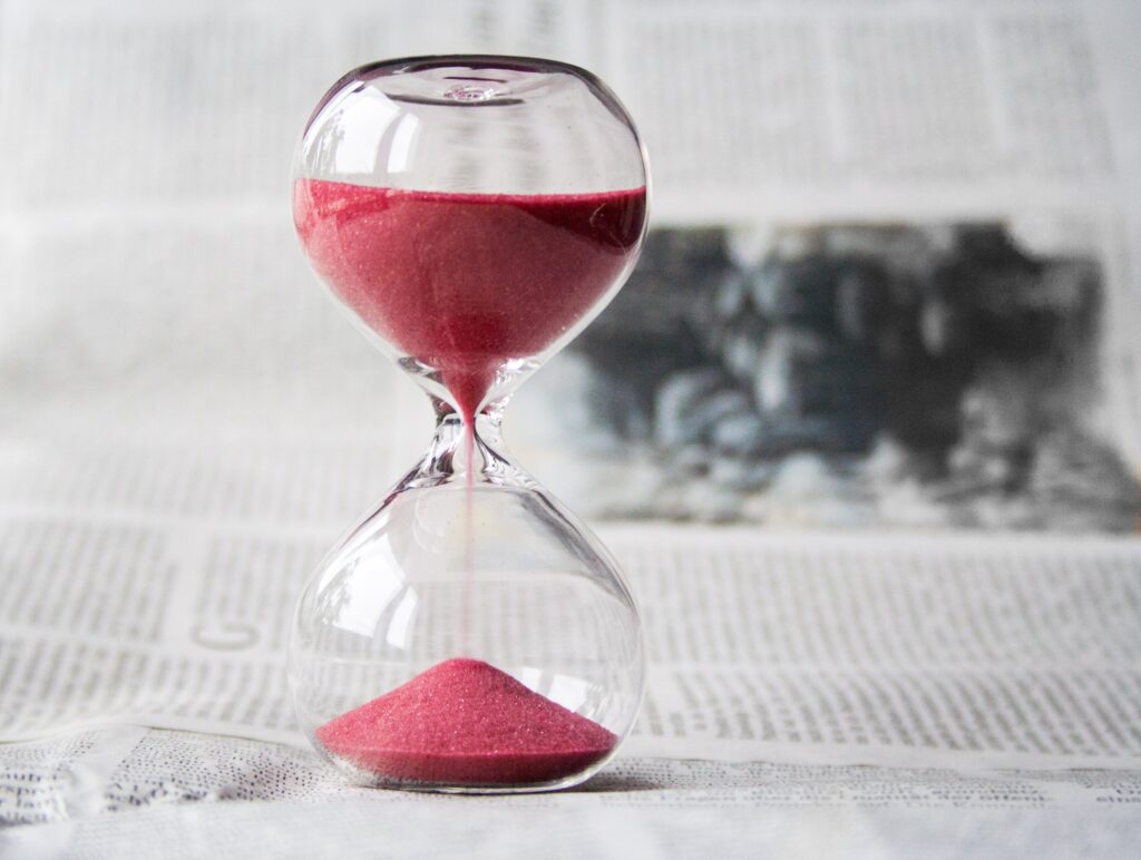 Hourglass with pink sand that sits on a newspaper.