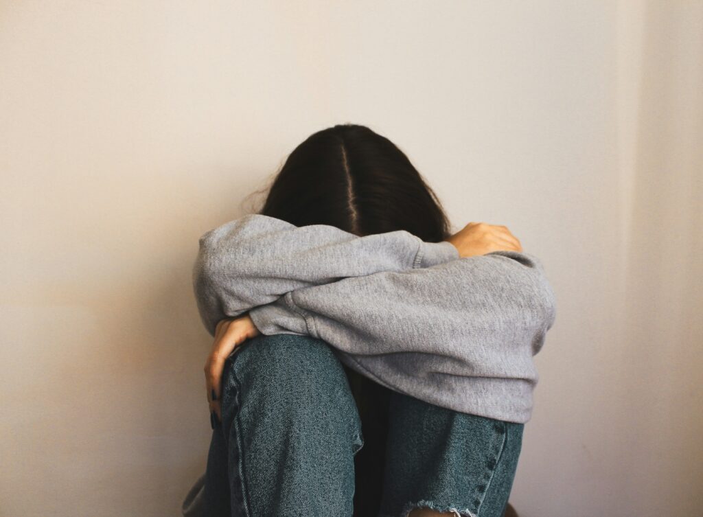 Woman sitting on the floor, arms wrapped around her head