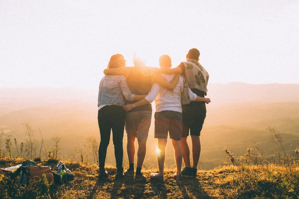 Four people with hands wrapped around each other, looking at a sunset.